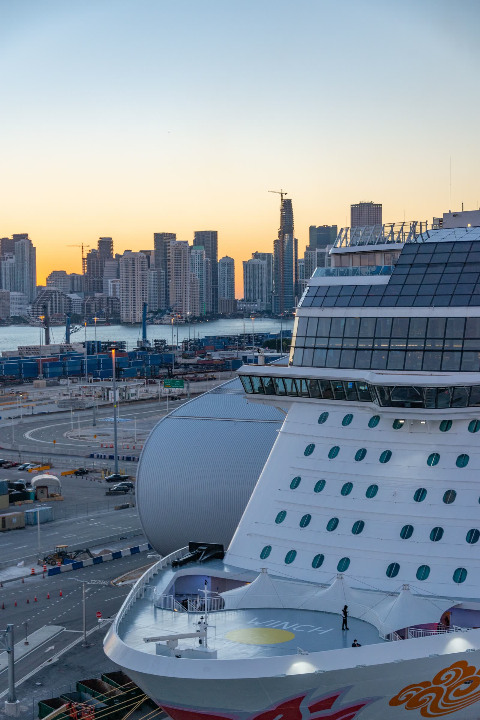 The bow of a cruise ship at PortMiami at sunset, the Miami skyline behind it