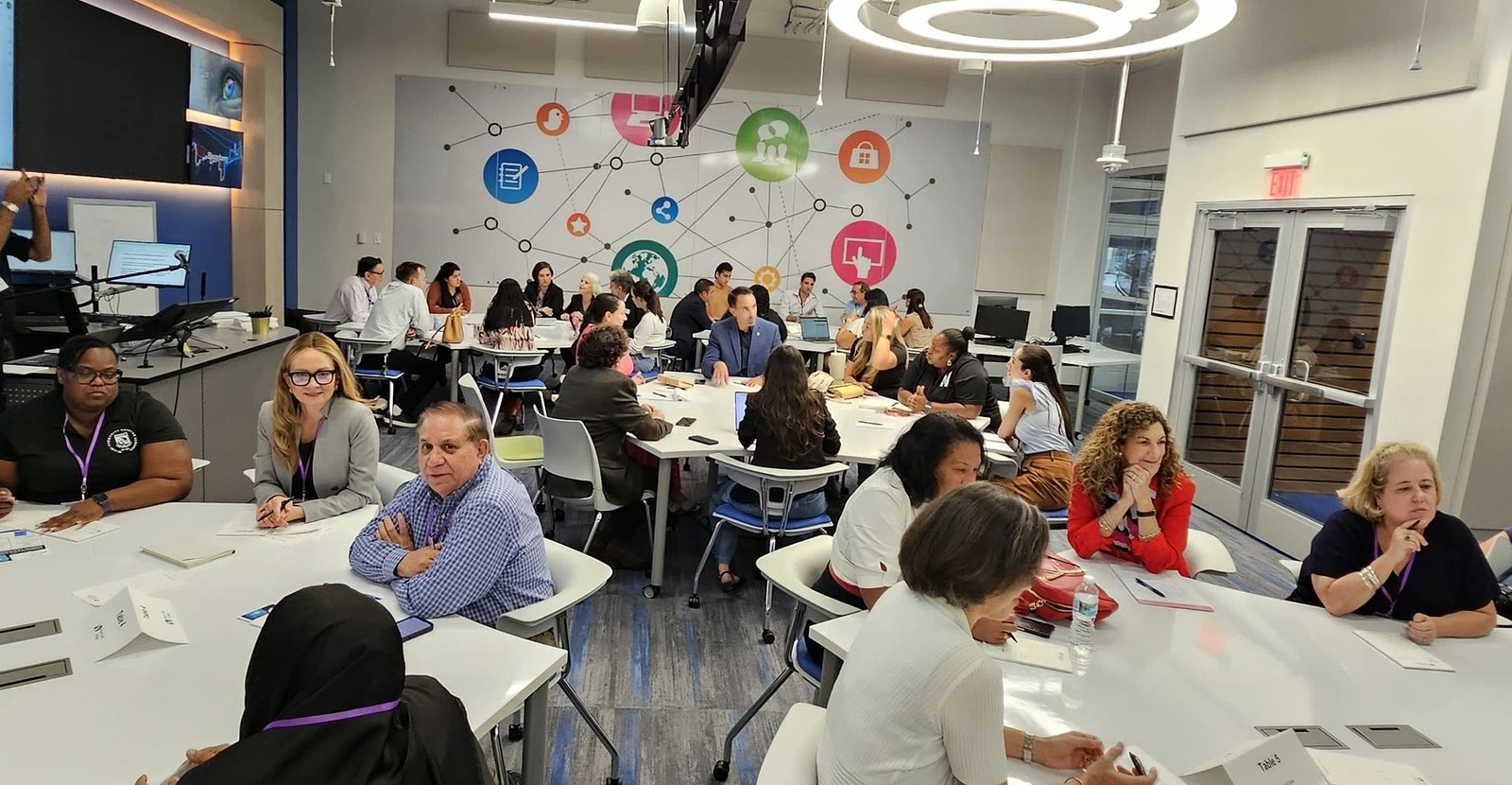 Roundtable participants in discussion at tables beneath a network mural